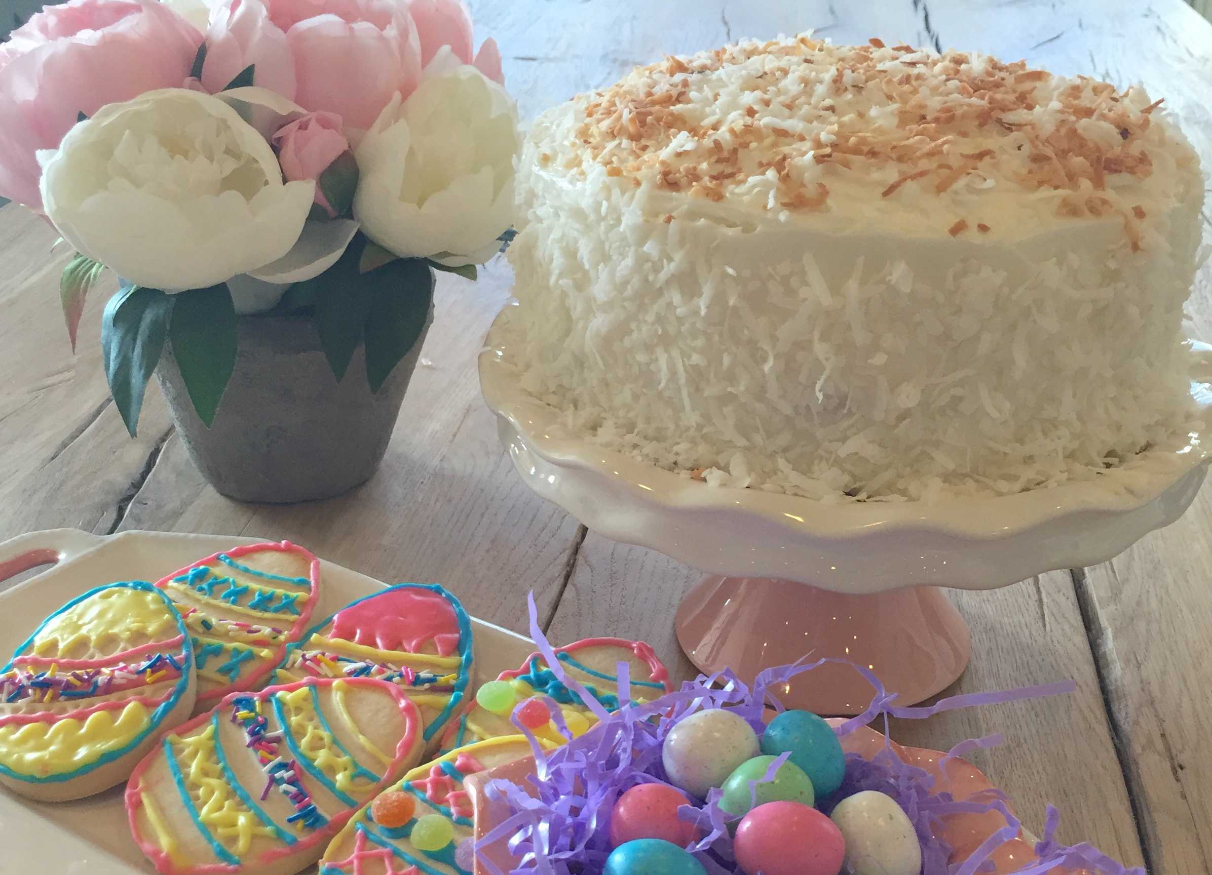 A watercolour still life in pale buttercream, soft pink, and warm vanilla tones, with rounded forms suggesting a frosted cake and delicate blossoms.